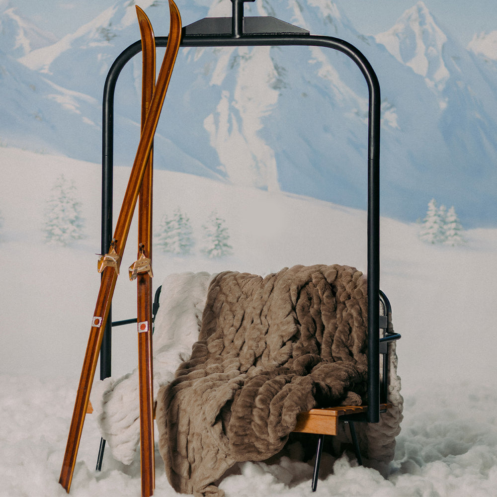 Ski lift chair with a blanket and wooden skis against a snowy mountain backdrop