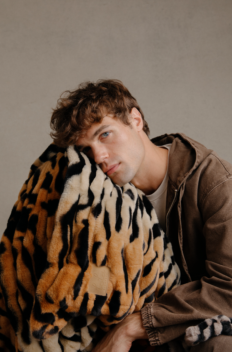 Man wrapped in a leopard print blanket against a neutral background