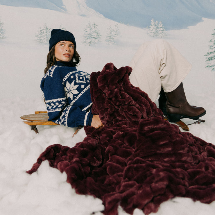 Woman sitting in the snow with a dark red fur blanket