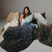 Woman sitting on a couch with a large, fluffy blanket draped over her