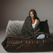 Woman wrapped in a blanket sitting on a brown leather couch against a gray background