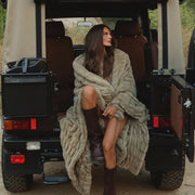 Woman wrapped in a blanket sitting in the back of an open jeep