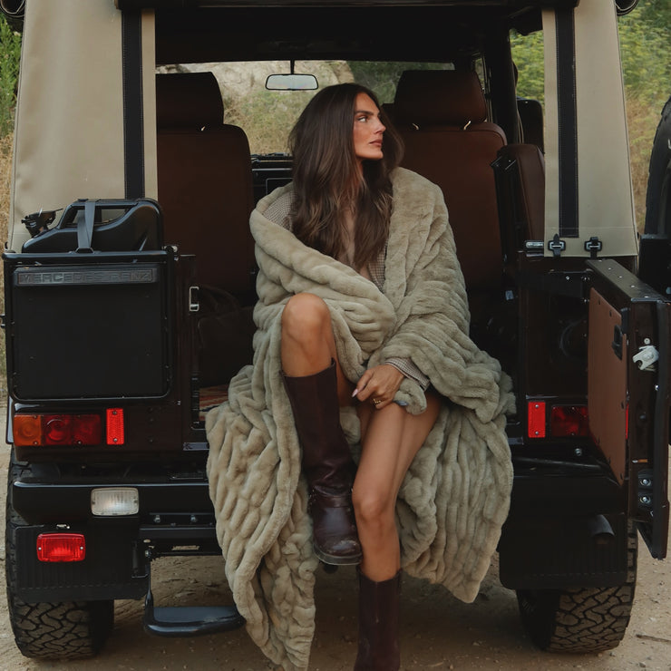 Woman wrapped in a blanket sitting in the back of an open jeep