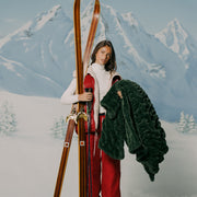 Person holding skis and a green jacket with a snowy mountain background